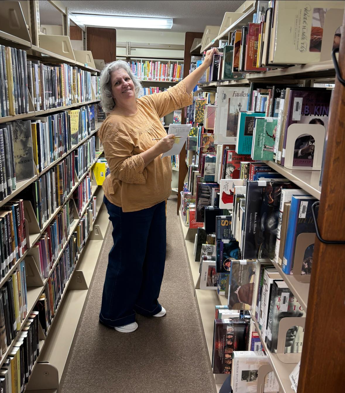 Mandy standing in a library aisle weeding books from the shelves.